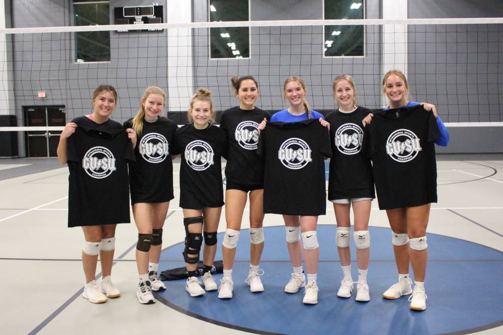 Students wearing and holding up championship shirts from a women's volleyball tournament